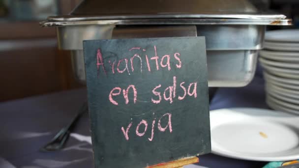 Duży metalowy garnek i czarny znak z różowym hiszpańskim tekstem na stole - Materiał filmowy, wideo