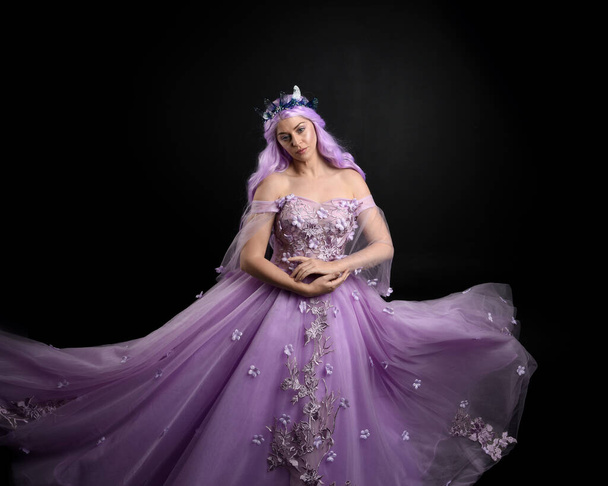 Retrato de cerca de la niña con vestido largo de bola de fantasía púrpura con corona de mariposa y pelo rosa, sobre un fondo de estudio oscuro. - Foto, imagen