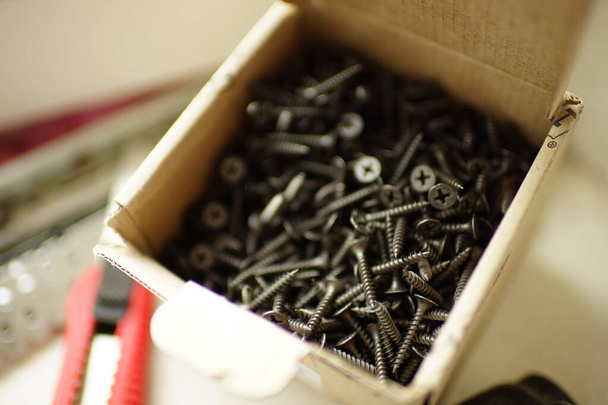 Un montón de nuevos tornillos autorroscantes negros en una caja - Foto, imagen