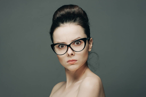 surprised woman with glasses naked shoulders gathered hair gray background - Photo, Image