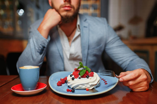 ケーキとカプチーノを飲みながらカフェに座っている若い男のクローズアップ - 写真・画像