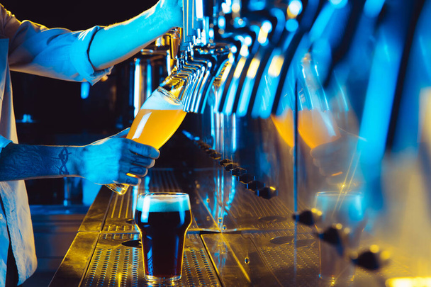 Jovem barman derramando cerveja lager da torneira ao vidro em luz de néon. - Foto, Imagem