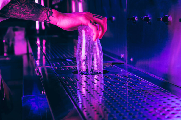 Αρσενικό χέρι πλύσιμο ποτήρι μπύρα στην παμπ σε πολύχρωμο νέον φως. - Φωτογραφία, εικόνα