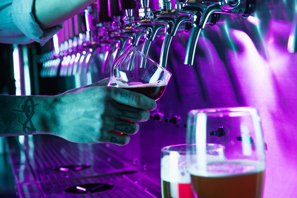 Cerveza de primer plano en barman mano en luz de neón multicilored. - Foto, Imagen