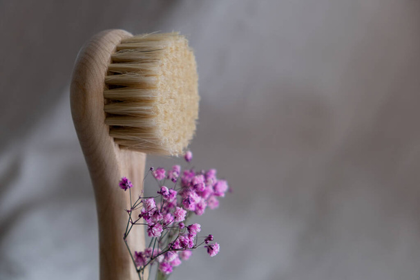 Facial massage brush with natural bristles on a linen background with bark and pink gypsophila flowers. eco friendly cosmetics concept.. - Photo, Image