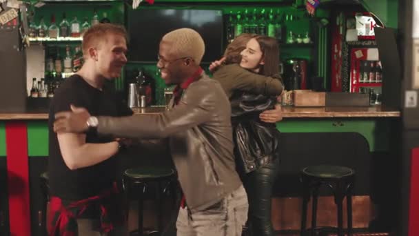 Plan moyen avec lenteur de jeunes amis diversifiés se rencontrant au pub irlandais la nuit, souriant tout en se saluant - Séquence, vidéo
