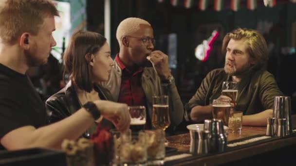 Vyötärö-up kuvamateriaalia onnellinen nuori ryhmä monikansallisia ystäviä hauskaa yhdessä istuu baarissa oluen juominen ja jutteleminen - Materiaali, video