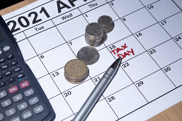 Φορολογική ημέρα εικόνα με ένα ημερολόγιο Απρίλιο ένα στυλό μια αριθμομηχανή σε κέρματα για τη φορολογική ώρα.     - Φωτογραφία, εικόνα