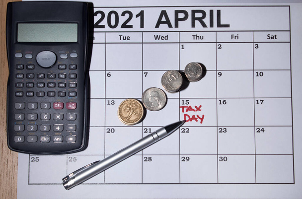 Изображение дня налогообложения с апрельским календарем ручка калькулятор в монетах для налогового времени.     - Фото, изображение