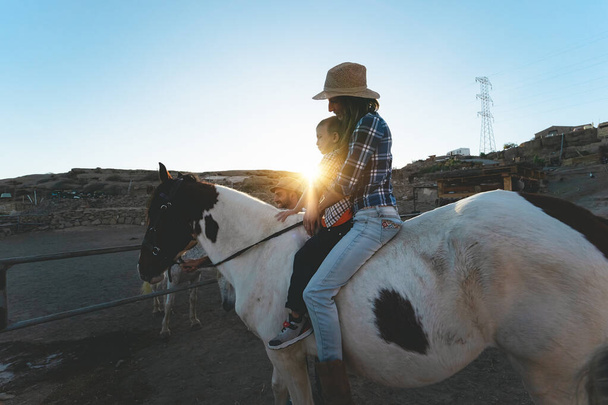 Feliz familia madre e hija divirtiéndose a caballo dentro del rancho - Foto, imagen