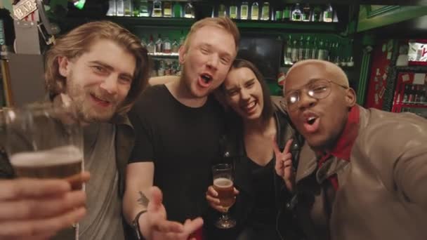 POV portátil con lentitud de alegres amigos multiétnicos con vasos de cerveza divirtiéndose en el bar por la noche tomando selfie en la cámara riendo y animando - Imágenes, Vídeo