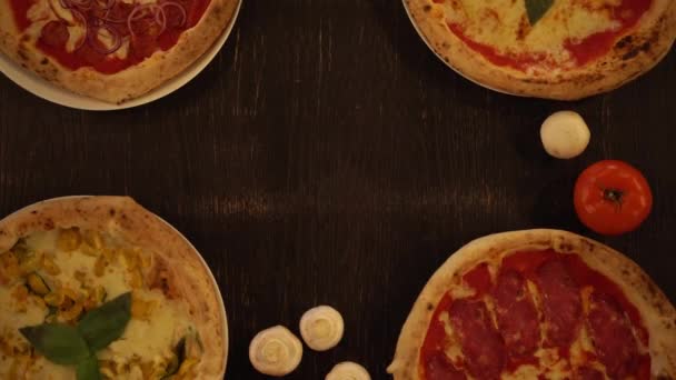 Mettere rucola calda e pizza al formaggio sul tavolo di legno. Vista dall'alto verso il basso della varietà di pizze su un tavolo di legno - Filmati, video