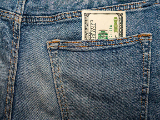 100-dolarowy banknot wystaje z tylnej kieszeni dżinsów. - Zdjęcie, obraz