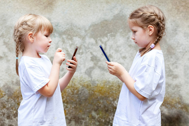 Zwei kleine Mädchen, Schwestern oder Freundinnen, die ihr Smartphone benutzen, Kinder, die mit ihren Mobiltelefonen einander gegenüberstehen. Kinder und moderne Technik, Sucht, Abhängigkeit, einfaches Lebensstilkonzept - Foto, Bild