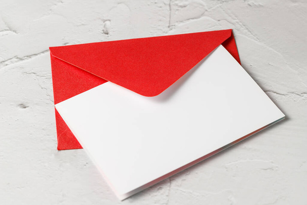Červená obálka s prázdnou papírovou kartou detailně na světlém kamenném pozadí. Mockup pohlednice s kopírovacím prostorem - Fotografie, Obrázek