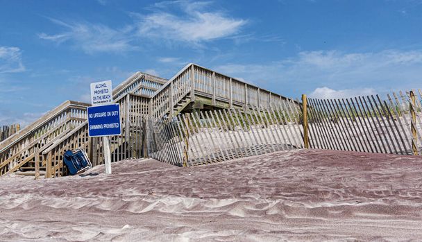 Fából készült lépcsőház a homokdűnék felett a Tűz-szigetek partján, alkoholos felirattal és szolgálatban lévő életmentő nélkül.. - Fotó, kép