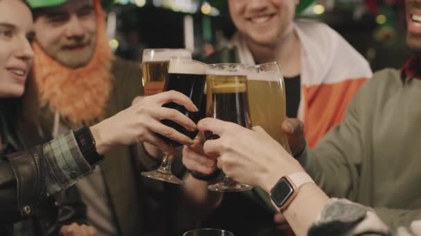 Средний крупный план с медлительностью молодых мультиэтнических компаний друзей в смешных зеленых ирландских костюмах тост кружки пива в честь Дня Святого Патрика в местном пабе - Кадры, видео