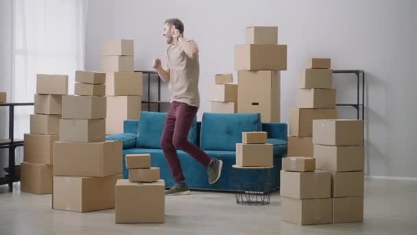 Young man have fun dancing in their new home. Very Happy Man Moves Into His New Apartment, Dances Excited. Guy Purchased New Home Ready to Start Unpacking Cardboard Boxes. - Footage, Video