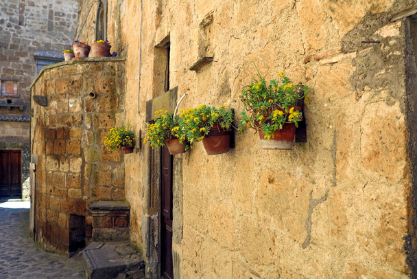 egy történelmi ház falán lógó sárga virágvázák Civita di Bagnoregio városában (Lazio) - Fotó, kép