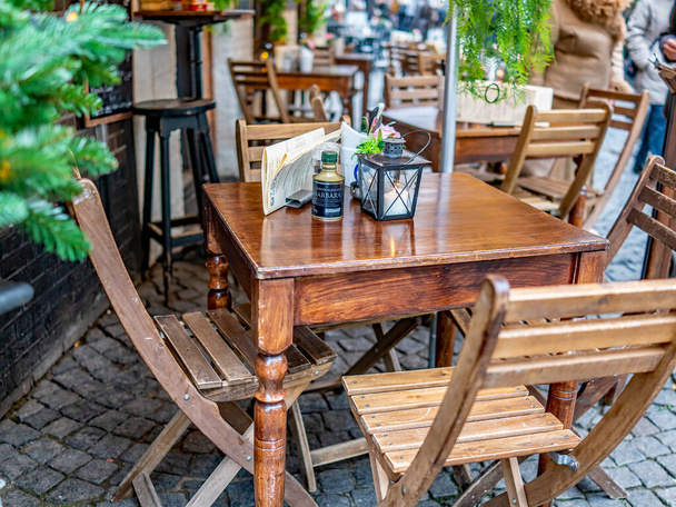 Επιλεκτική εστίαση σε ένα υπαίθριο τραπέζι και καρέκλες ανάμεσα σε μια σειρά από τραπέζια και καρέκλες στο δρόμο έξω από μια παμπ στην πόλη του Μάαστριχτ, Ολλανδία - Φωτογραφία, εικόνα