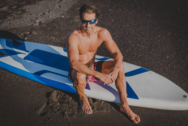 um jovem desportista pratica paddle surf na praia sob um céu azul - Foto, Imagem