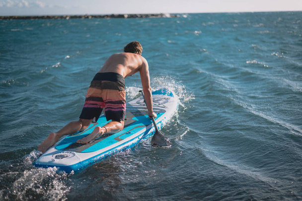 młody sportowiec ćwiczy surfing na plaży pod błękitnym niebem - Zdjęcie, obraz