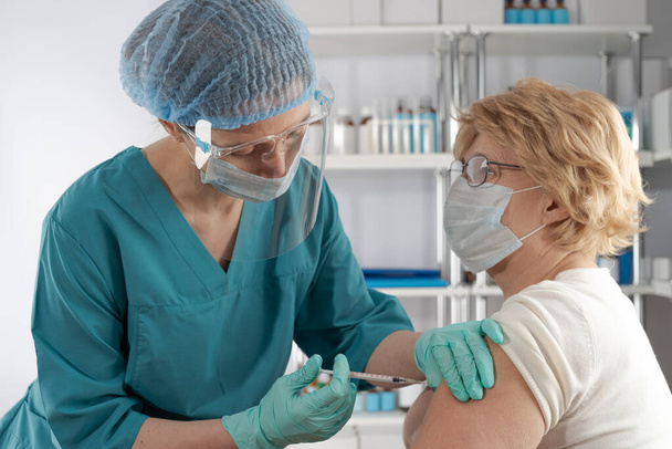 Vacuna inyectable profesional médica femenina a una mujer adulta mayor. Caso de salud hospital al aire libre - Foto, imagen