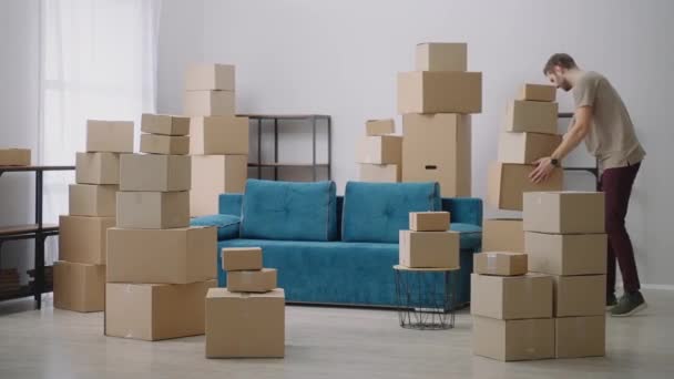 A fiatalember kartondobozokban mozog. Fiatal férfi költözik az új lakásba. Egy férfi ül egy kanapén egy új lakásban, miután beköltözött. - Felvétel, videó