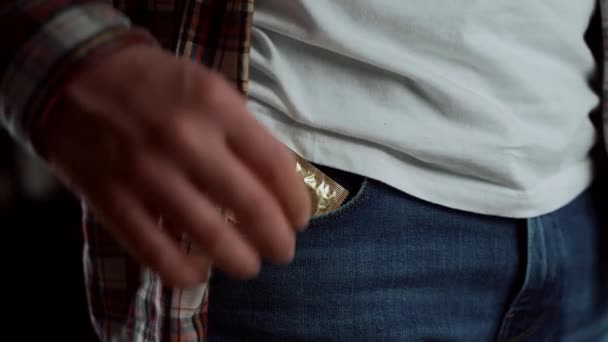 Close-up van een jongeman die condoom uit zijn broekzak haalt in jeans. Denk aan bescherming. Veilige seks, AIDS. Ik haal de gouden condoomkleur tevoorschijn. Veiligheid seksconcept. Anticonceptie. Anticonceptiemiddel. Wereld Aids Dag - Video