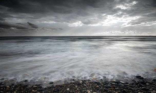 Θαλασσινά κύματα πέφτουν στην ακτή με πέτρες ενάντια στον θυελλώδη συννεφιασμένο ουρανό. Χειμώνας, Κύπρος Λεμεσού - Φωτογραφία, εικόνα