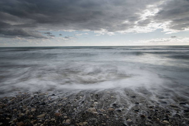 Θαλασσινά κύματα πέφτουν στην ακτή με πέτρες ενάντια στον θυελλώδη συννεφιασμένο ουρανό. Χειμώνας, Κύπρος Λεμεσού - Φωτογραφία, εικόνα
