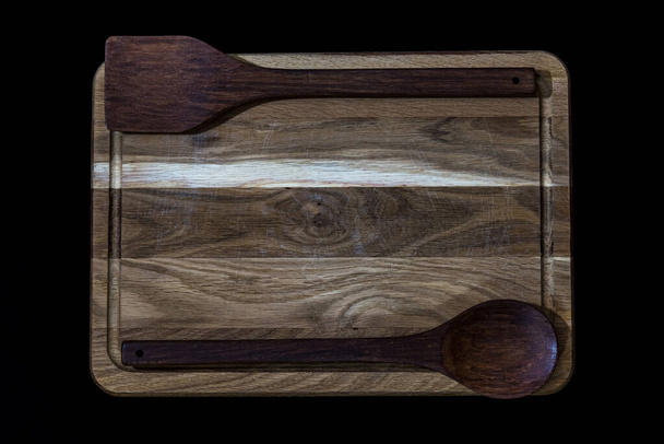Tablero de cocina de madera de roble sobre fondo negro con cuchara de madera y espátula de cocina. - Foto, Imagen