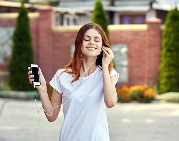 весела жінка в білій футболці на вуличній музиці з навушниками, що йдуть
 - Фото, зображення