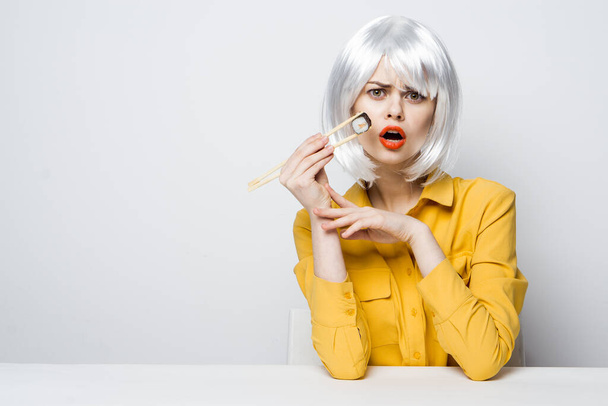 pretty woman in yellow shirt white wig sushi rolls eating - Photo, Image