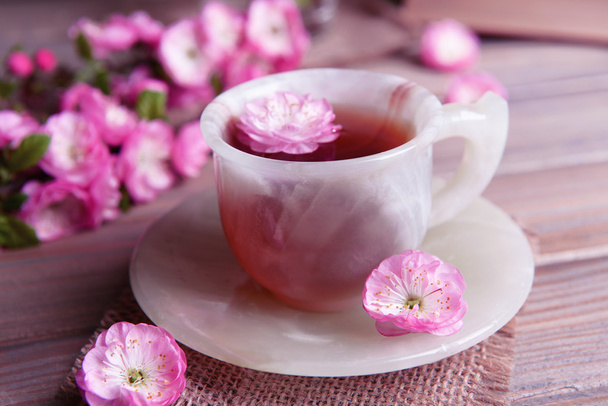 Beautiful fruit blossom with cup of tea on table on grey background - Foto, afbeelding