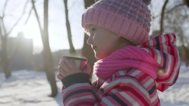 Sonriente niña niño bebiendo té de bebida caliente de la taza, tratando de mantener el calor en el bosque parque de invierno - Imágenes, Vídeo