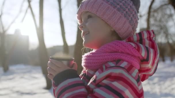 Kind trinkt Heißgetränk Tee aus Tasse auf verschneiter Straße im Winterpark, Weihnachtsferien - Filmmaterial, Video