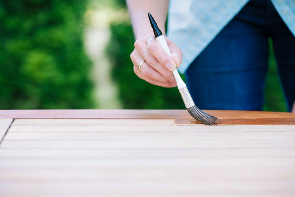 młoda kobieta malująca drewniany, egzotyczny drewniany stół w ogrodzie pędzlem - płytka głębia ostrości - Zdjęcie, obraz