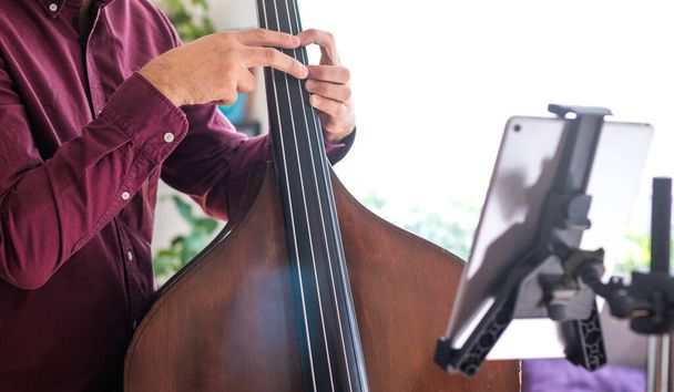 Young man teaching live music with his tablet. He teaches how to play the double bass - Photo, Image