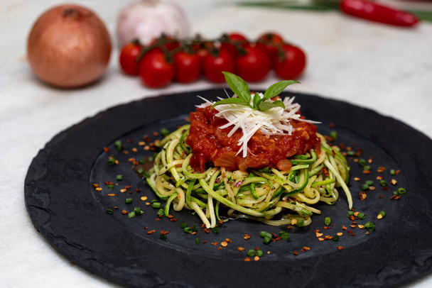 Zucchini spaghetti met gedroogde peperoni peper, rode saus en geraspte Parmezaanse kaas - Foto, afbeelding