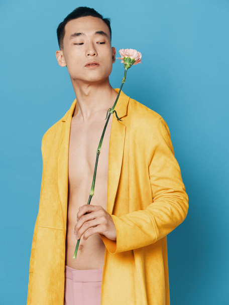 Romantique asiatique homme avec une fleur dans un manteau jaune sur un fond bleu - Photo, image