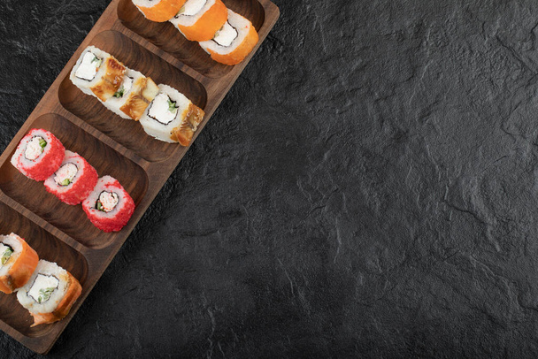 Drewniana płyta tradycyjnych bułek sushi na czarnym stole - Zdjęcie, obraz