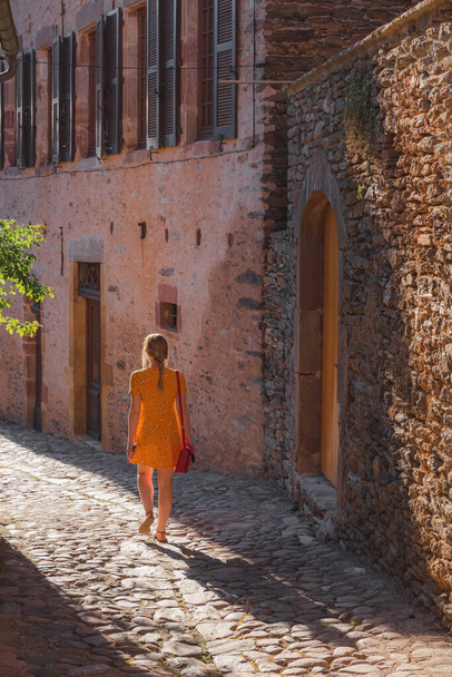Eine junge Touristin im Sommerkleid erkundet eine Feldstraße im malerischen und charmanten mittelalterlichen französischen Dorf Conques, Aveyron Occitanie Frankreich. - Foto, Bild