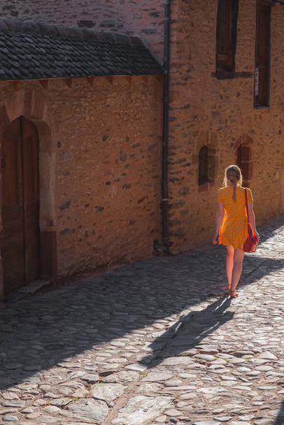 Eine junge Touristin im Sommerkleid erkundet eine Feldstraße im malerischen und charmanten mittelalterlichen französischen Dorf Conques, Aveyron Occitanie Frankreich. - Foto, Bild