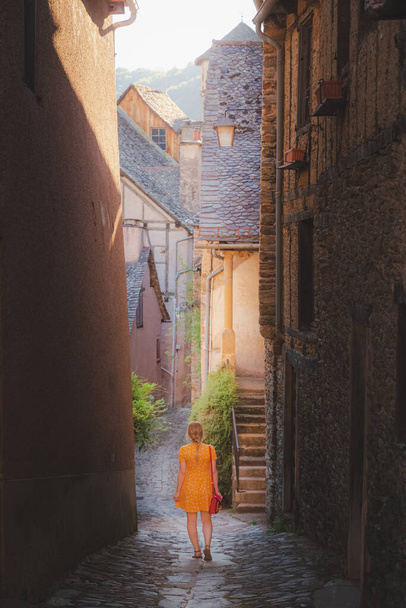 Una giovane turista in abito estivo esplora una stradina di campagna nel pittoresco e affascinante villaggio medievale francese di Conques, Aveyron Occitanie Francia. - Foto, immagini