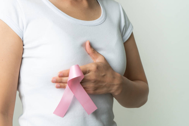 ruban d'insigne rose sur la main de la femme touchant la poitrine pour soutenir la cause du cancer du sein. concept de sensibilisation au cancer du sein - Photo, image