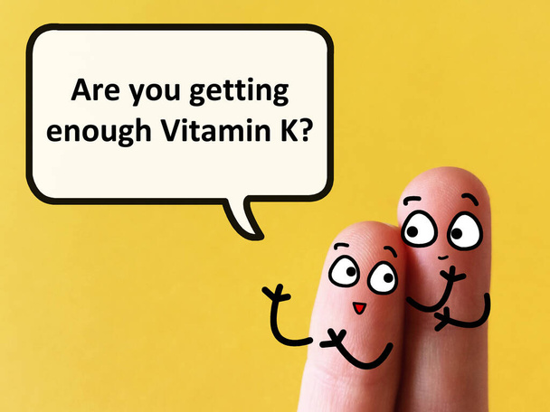Dos dedos están decorados como dos personas. Uno de ellos está preguntando a otro si está recibiendo suficiente vitamina K. - Foto, imagen