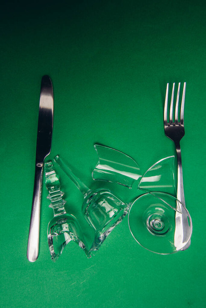 broken glass on a plate green napkin fork with knife wooden background - Photo, Image