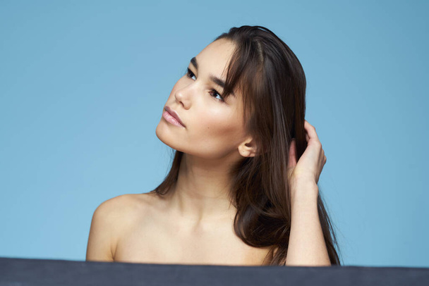 brunette met blote schouders cosmetica close-up huidverzorging blauwe achtergrond - Foto, afbeelding