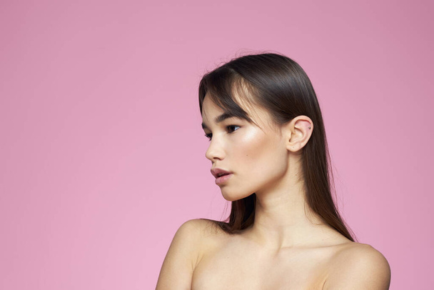 Donna con spalle nude cura dei capelli trucco pelle pulita sfondo rosa - Foto, immagini